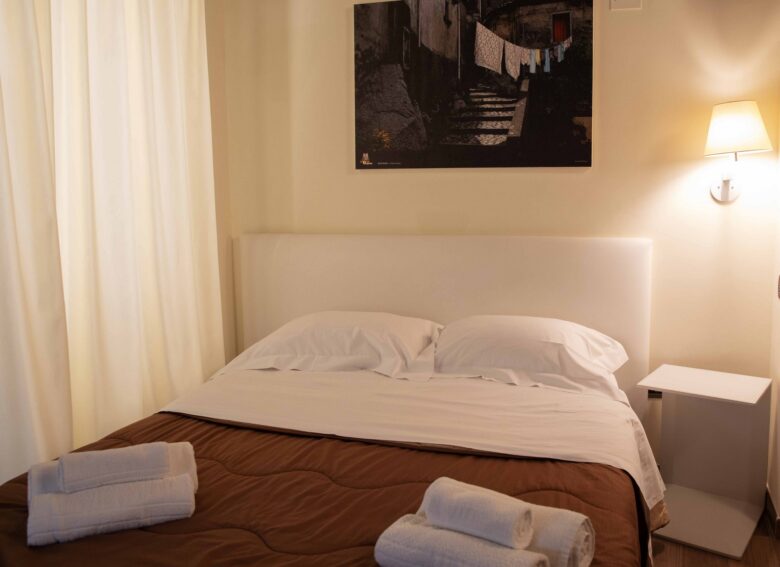 Camera matrimoniale 101 Hotel Sant’Anna Borgo Ospitale con letto matrimoniale, lampada da parete e fotografia del borgo sopra la testiera